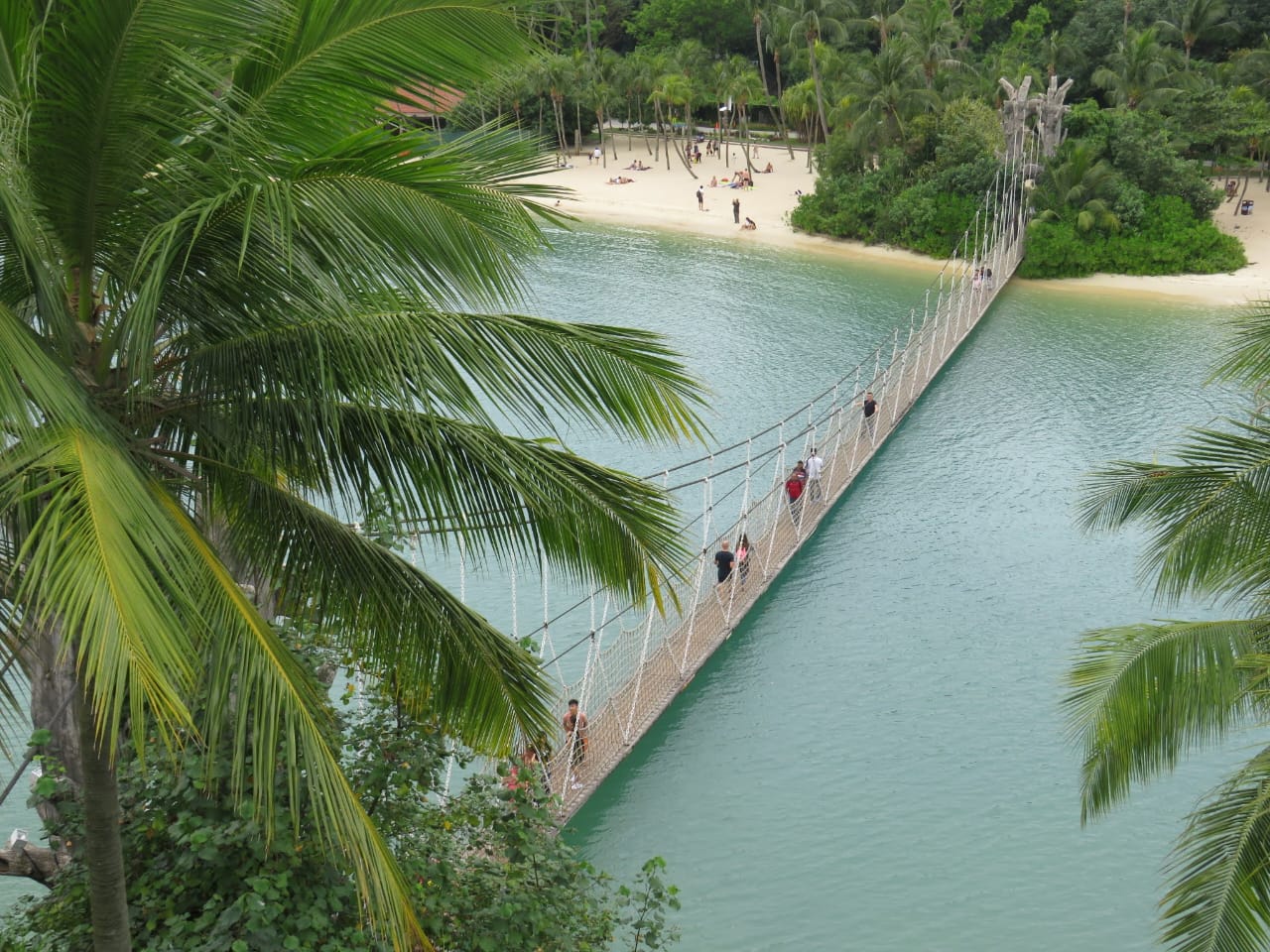 Suspension bridge over turquoise water with tropical landscaping and beach