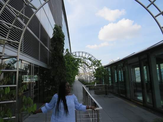 Anike on a futuristic covered walkway with architectural elements and greenery