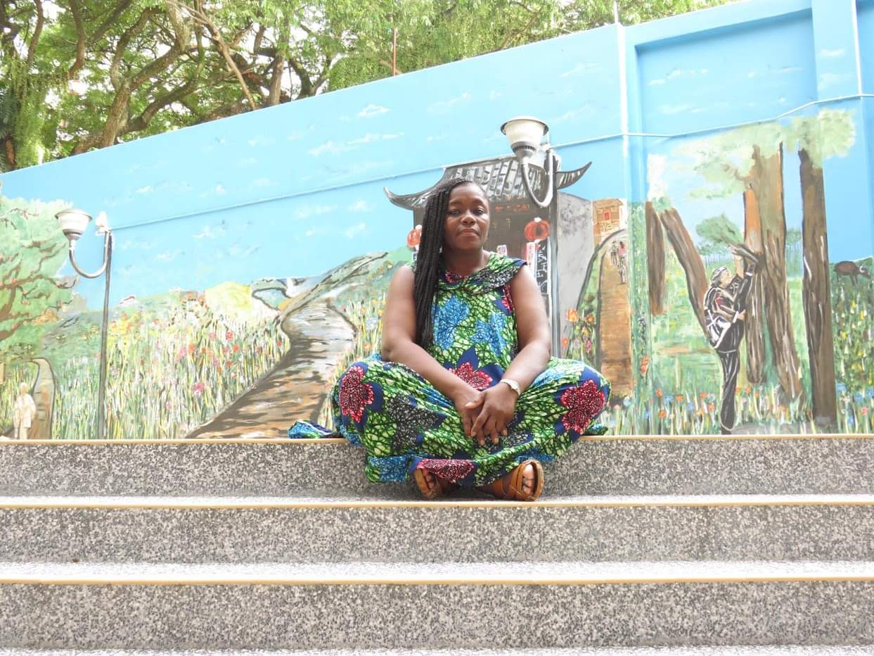 Anike sitting on steps in front of a colorful mural depicting Chinese cultural scenes