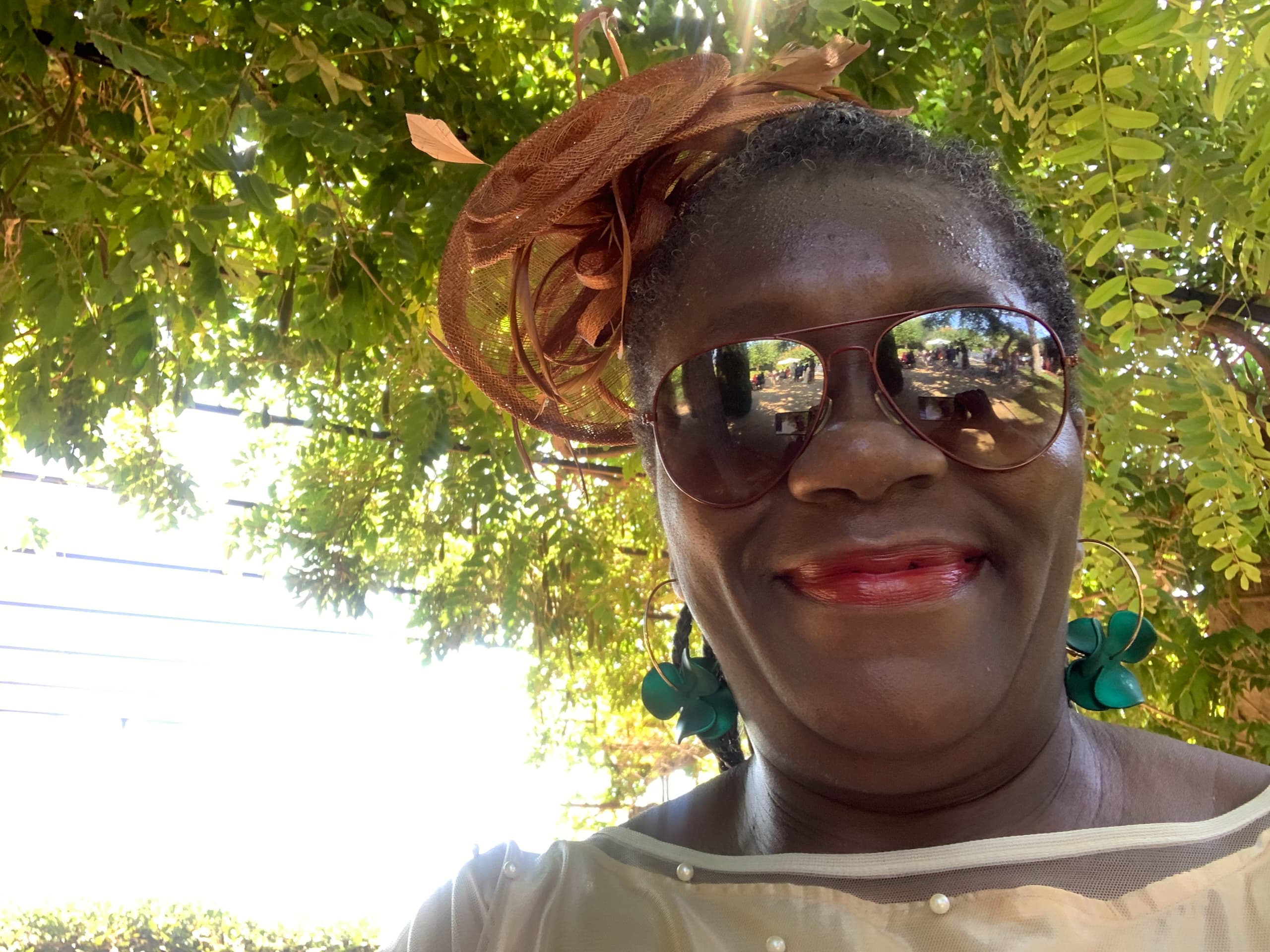Anike in sunglasses and brown headwrap under lush green foliage in Barcelona