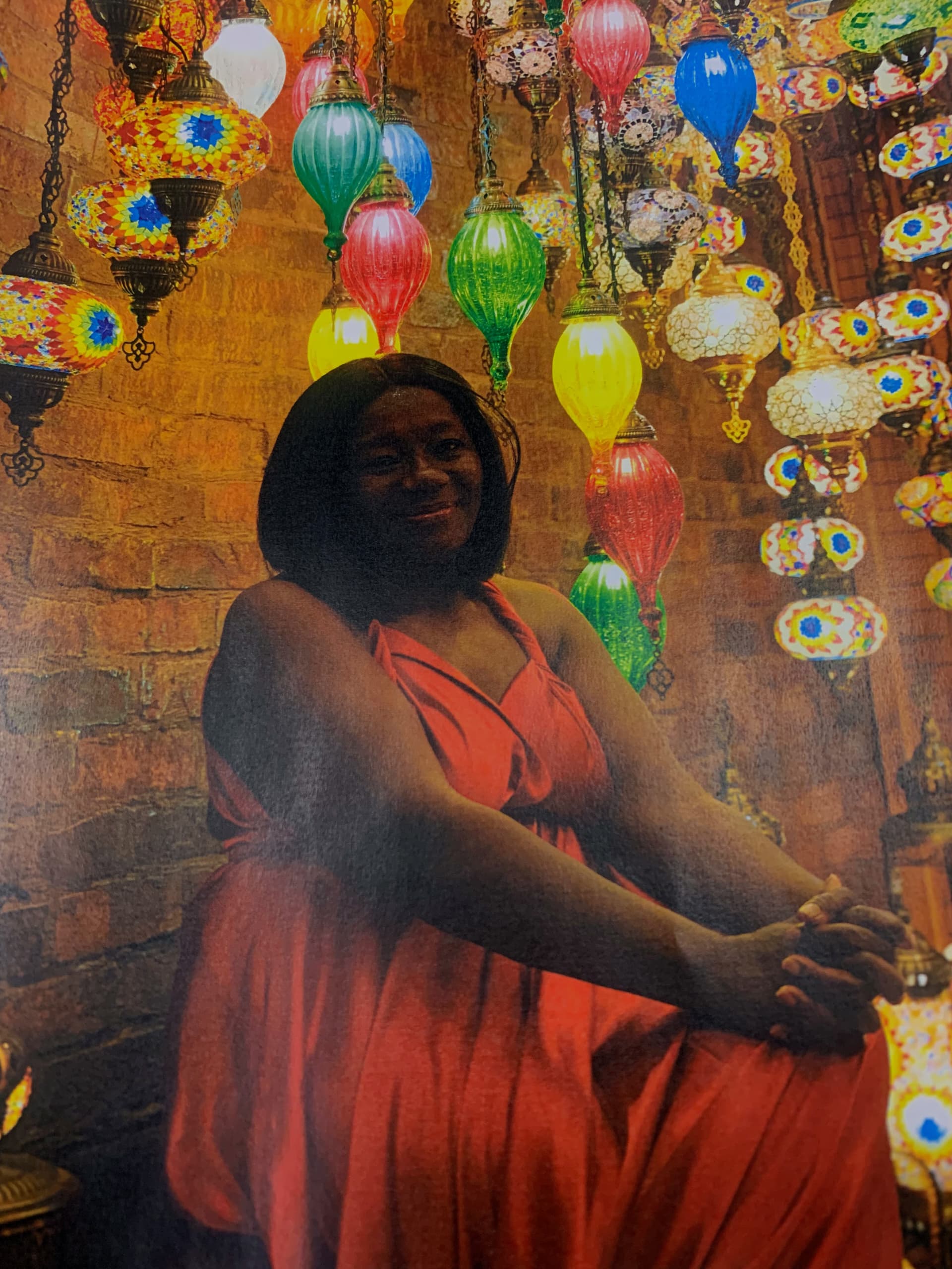 Anike sitting and smiling among colorful Turkish mosaic lamps